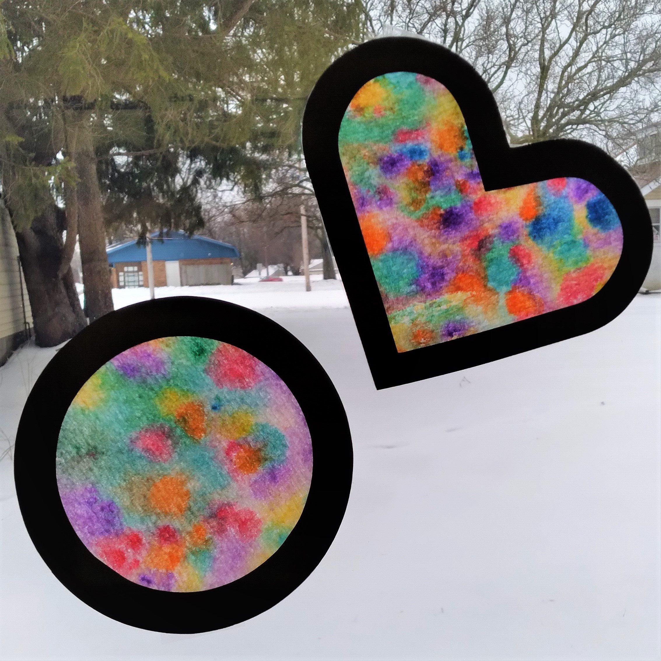 Colorful heart and circle with black borders on a window with snow in the background