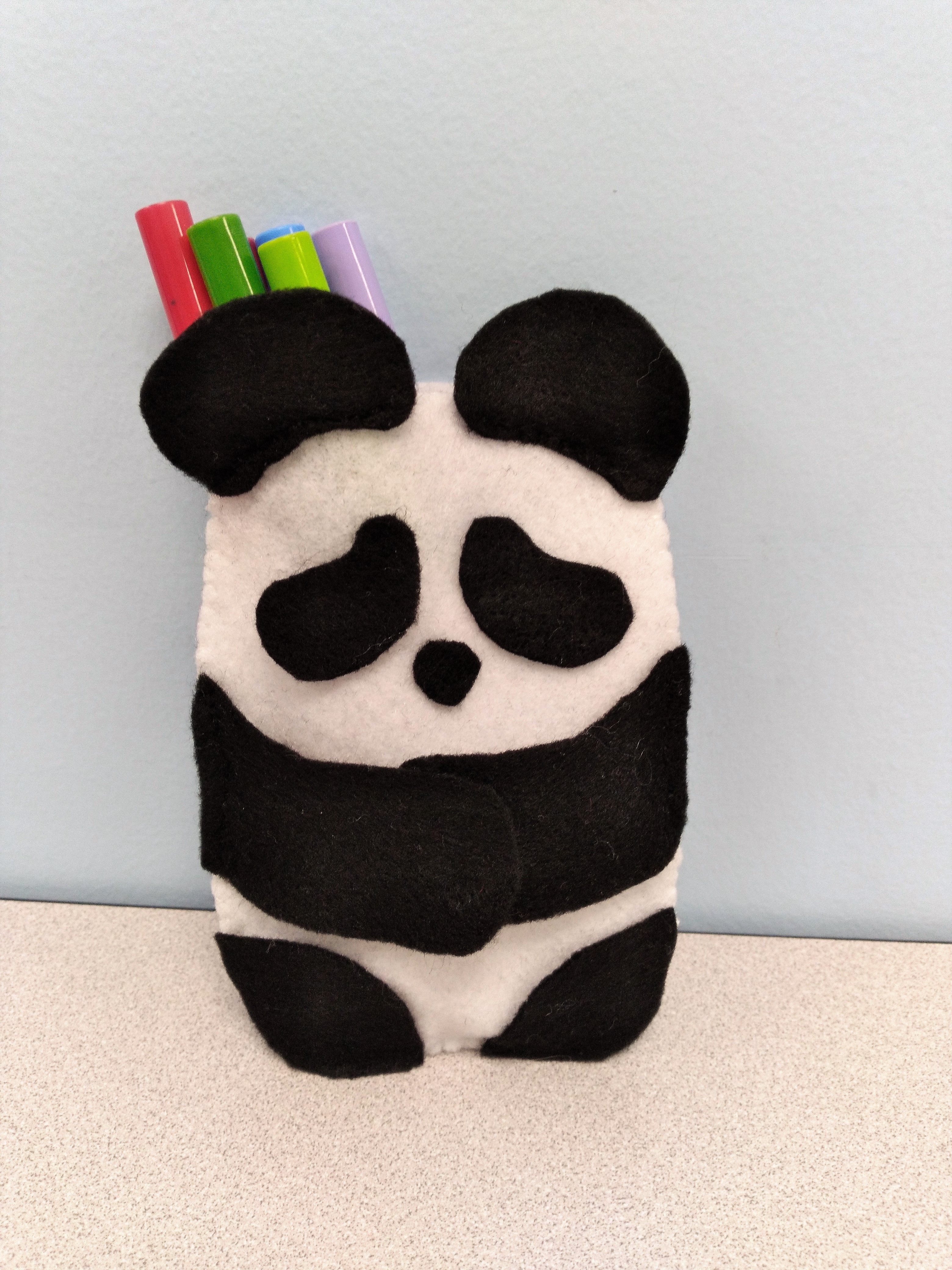 black and white image of a felt panda shaped pouch holding markers