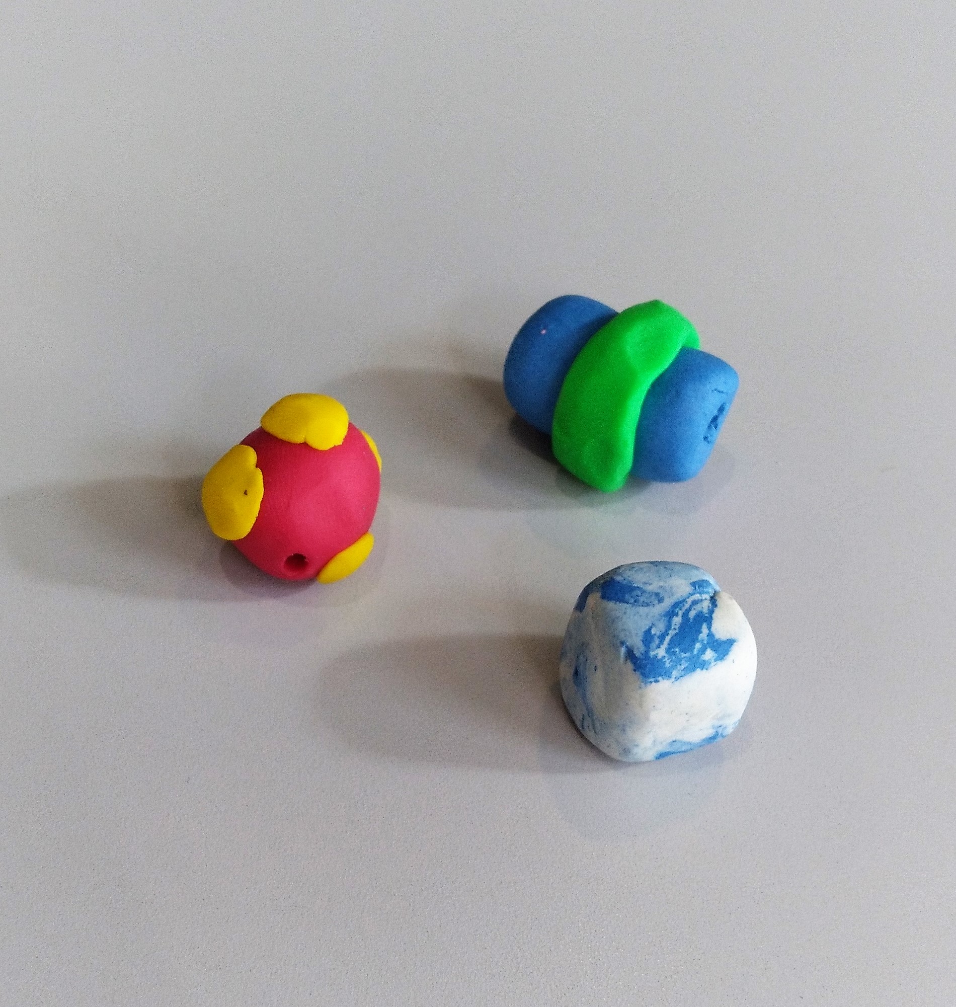 Three clay beads, red and yellow, white and green, and blue and white
