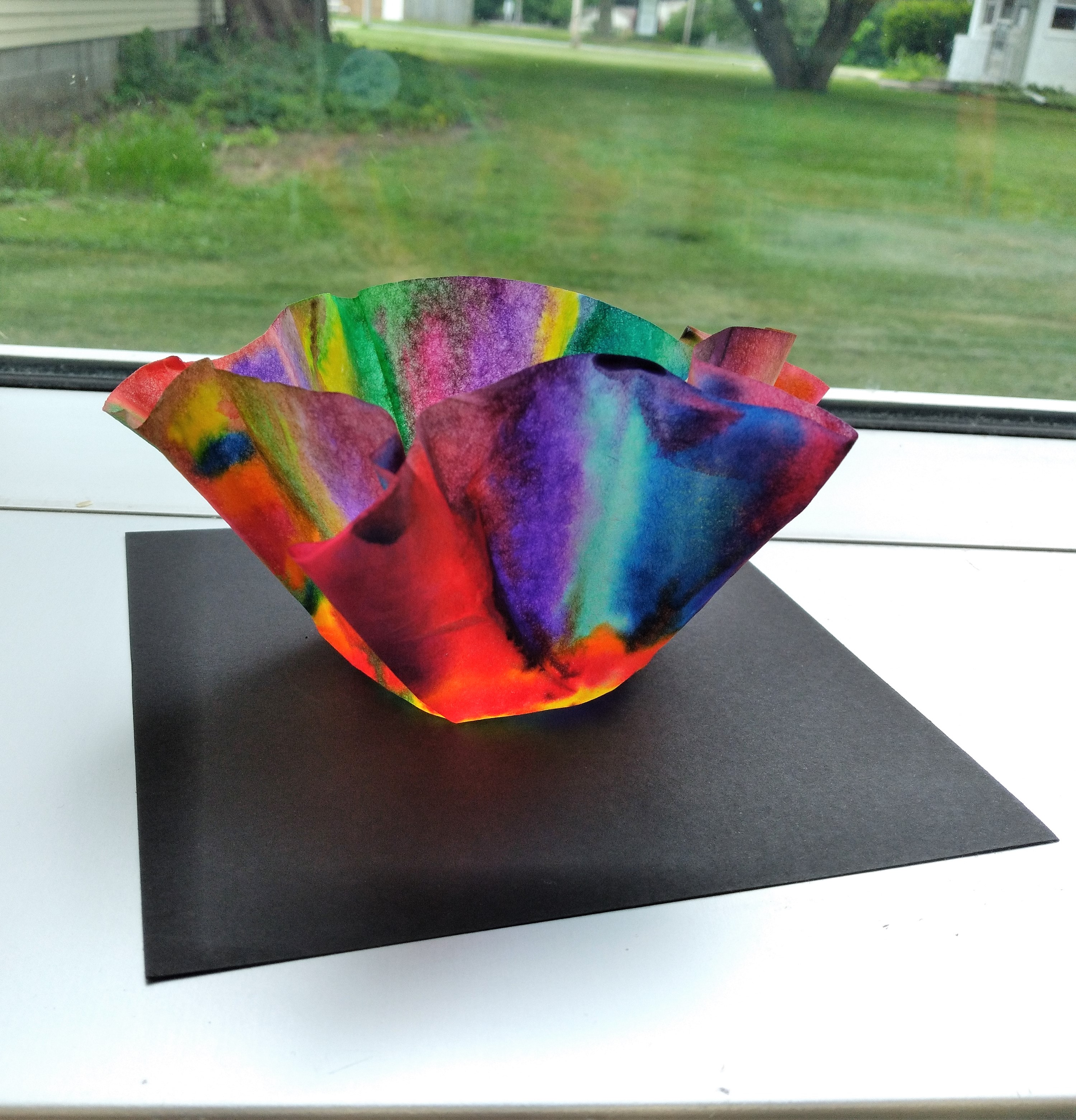 a colorful bowl or vase against a black base in front of a window