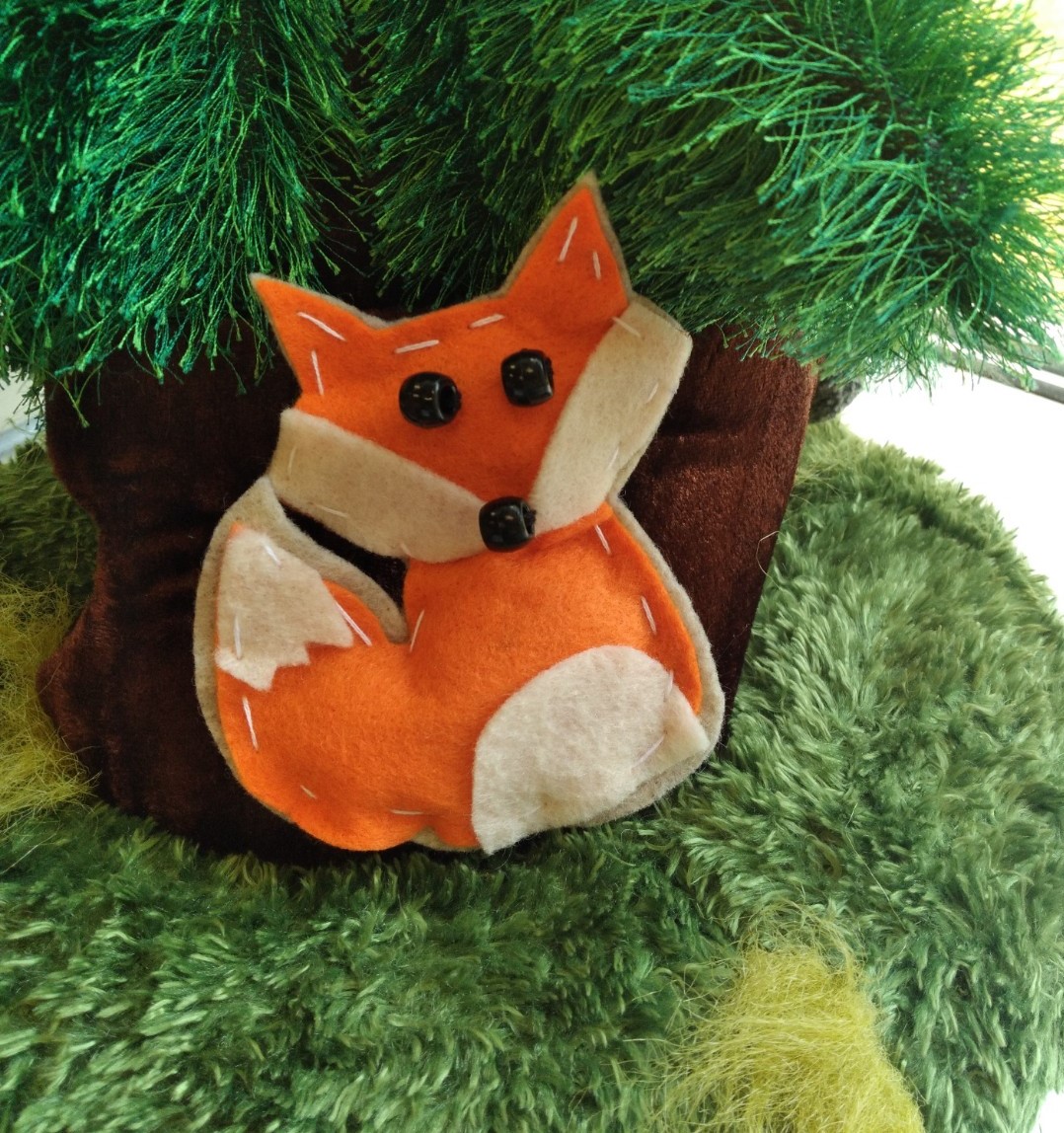 Orange felt fox resting on green tree