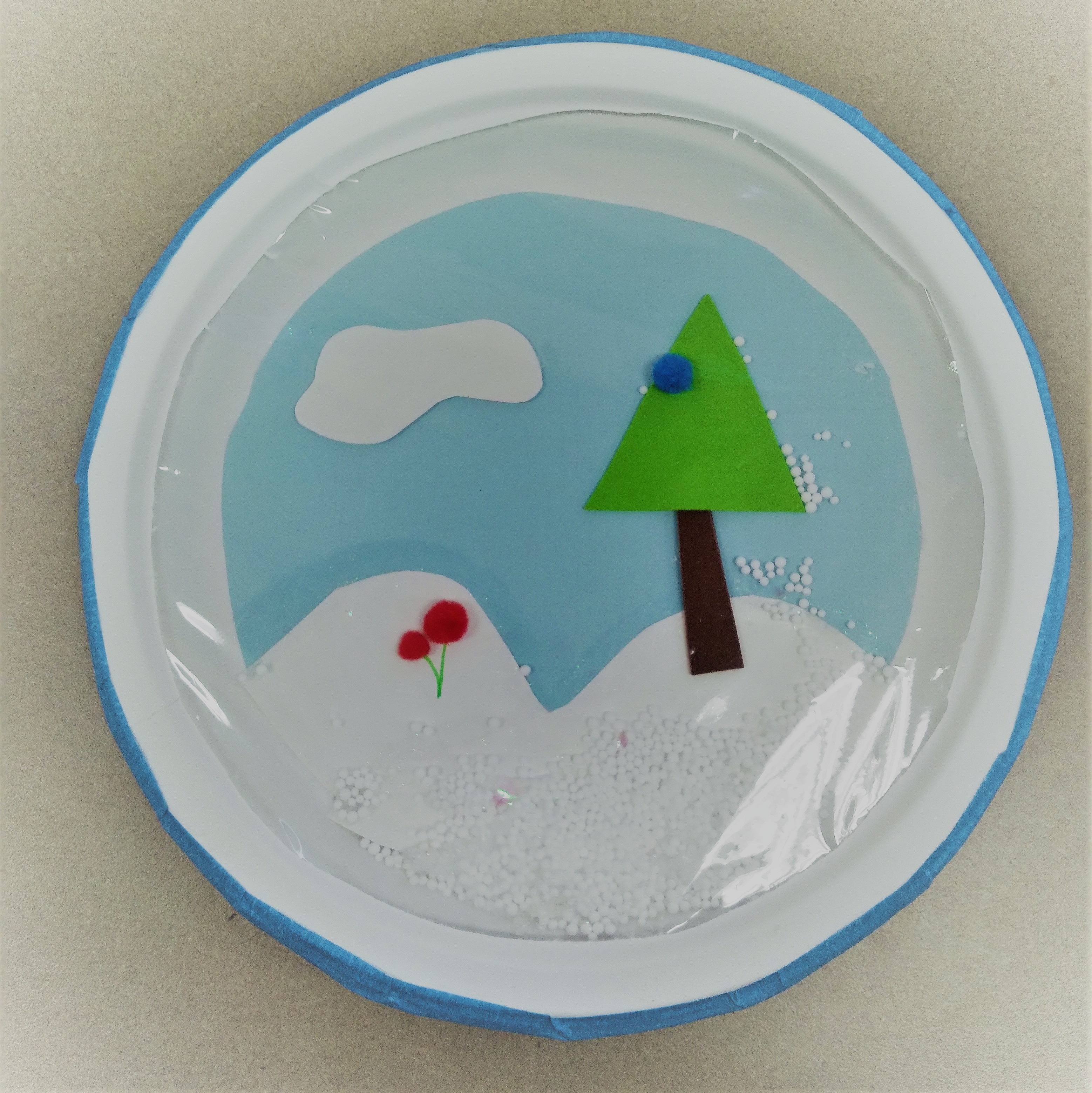 paper plate with trees and snowly landscape with plastic wrap over it