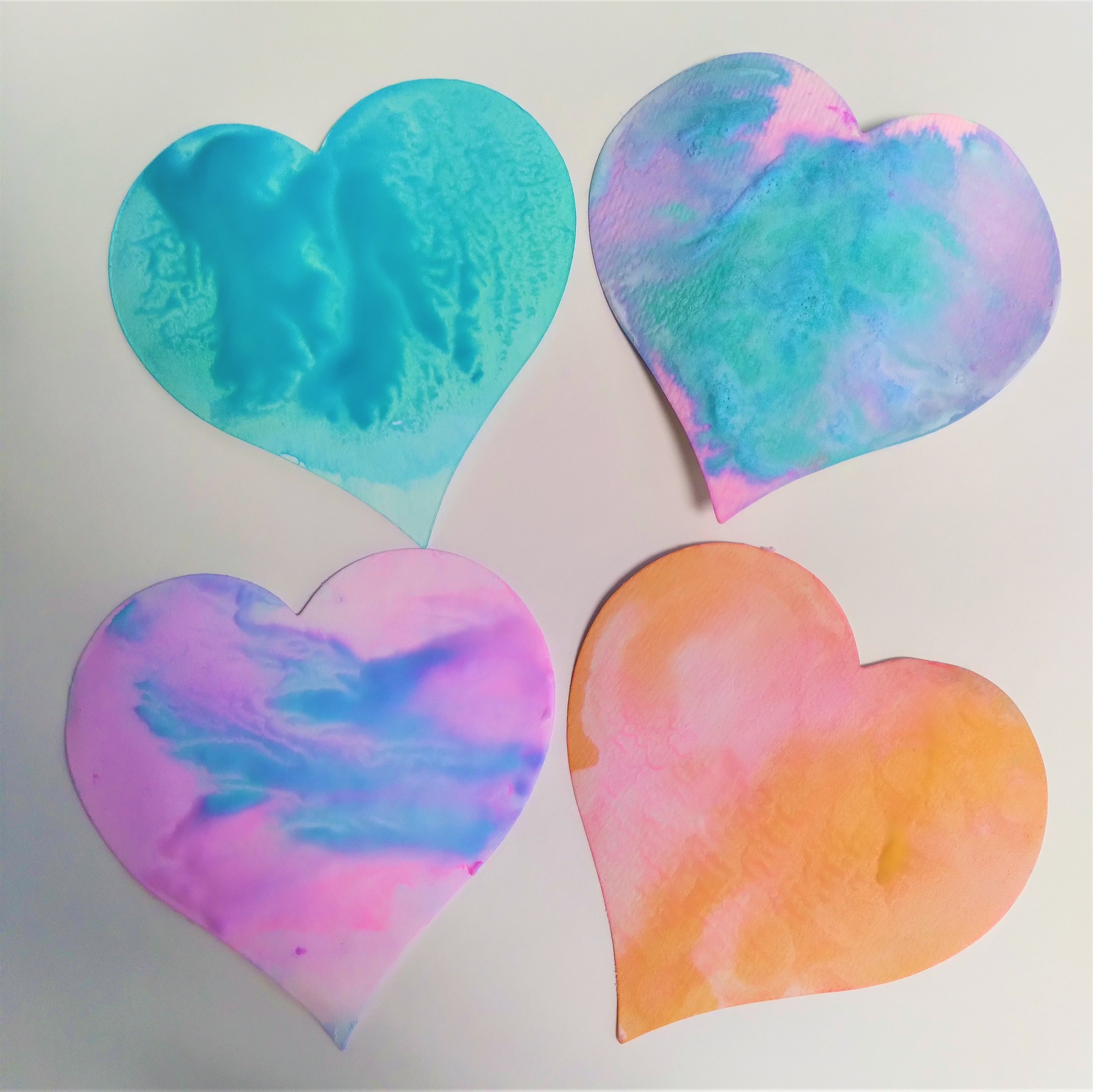 four watercolored paper hearts in blue, orange, pink and purple