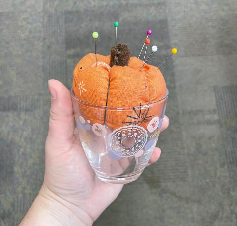 Sew Fun - Pumpkin Spice Pincushion: Image - hand holding a teacup containing a stuffed pumpkin with pins