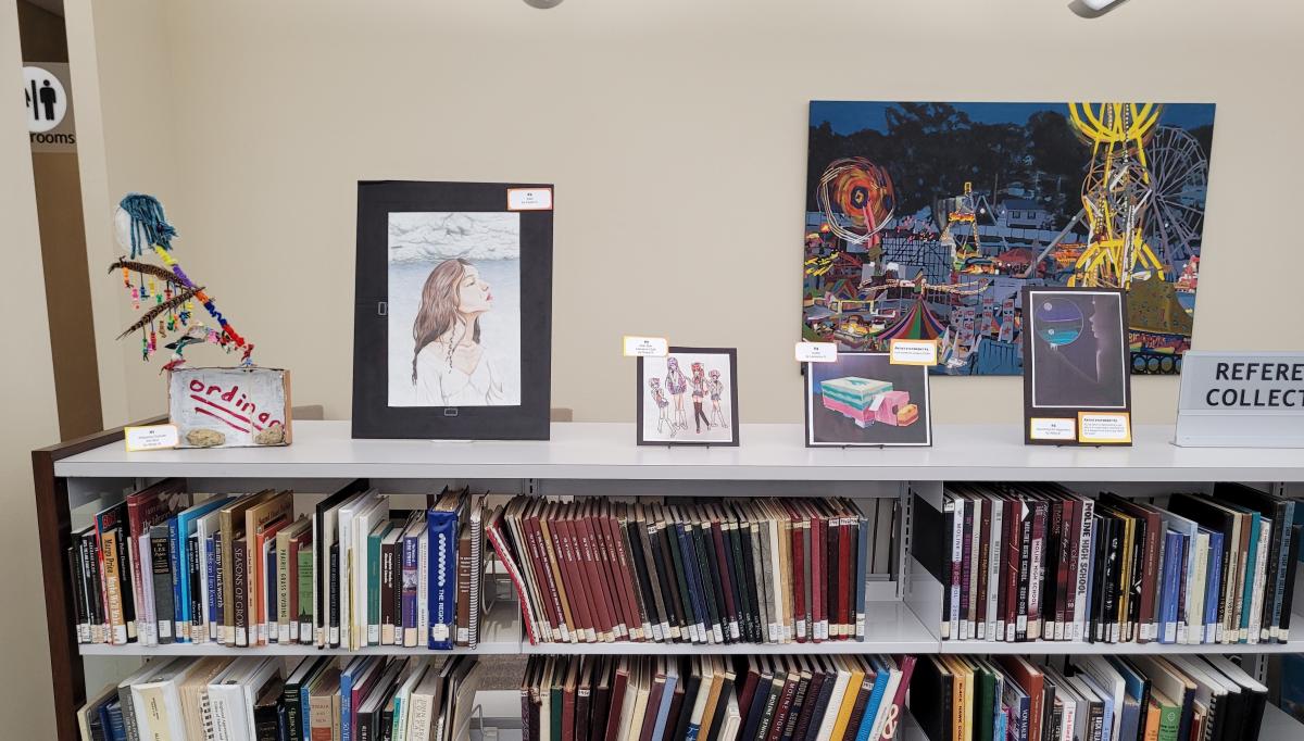 art pieces on library shelf with colorful painting in background